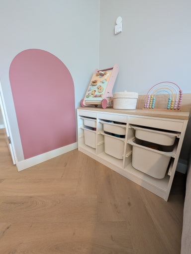 Rincón infantil con una superficie rosa en la pared y un mueble para juguetes